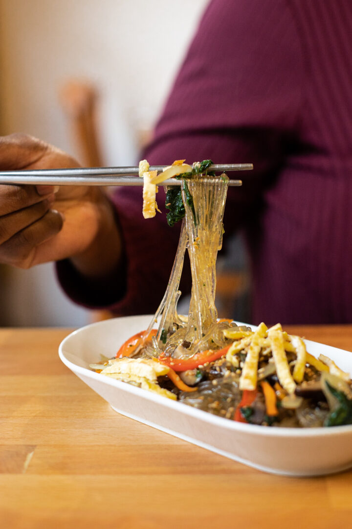 une personne prend des japchae avec des baguettes